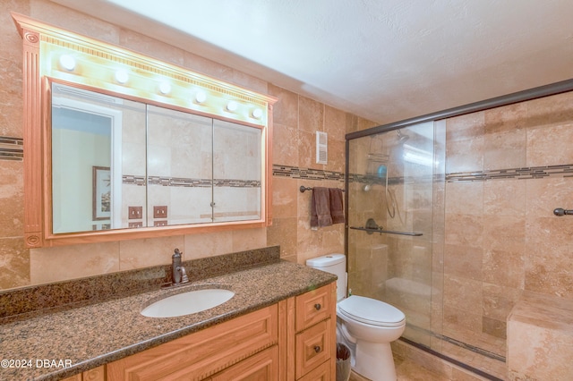 bathroom with tile walls, an enclosed shower, vanity, and toilet