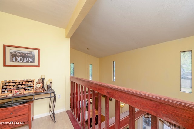 corridor featuring vaulted ceiling, light hardwood / wood-style floors, and a textured ceiling