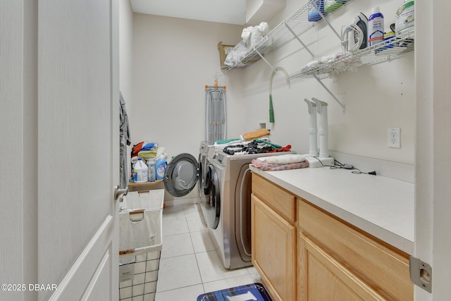 clothes washing area featuring washer and dryer, light tile patterned floors, and cabinets