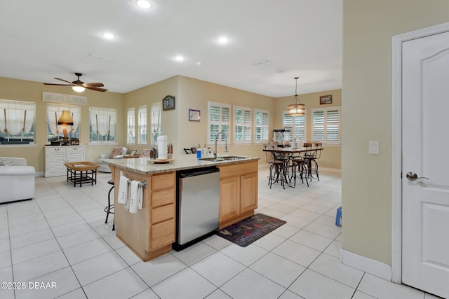 kitchen featuring light stone counters, sink, light brown cabinets, a center island with sink, and dishwasher