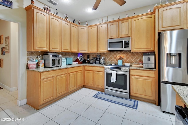 kitchen with tasteful backsplash, light stone countertops, light tile patterned flooring, and appliances with stainless steel finishes