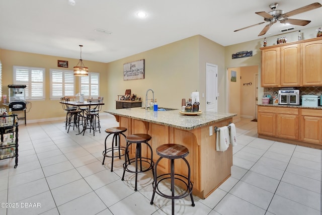 kitchen featuring pendant lighting, a kitchen island with sink, sink, light tile patterned floors, and light stone counters