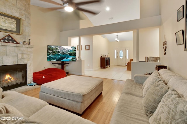 living room with ceiling fan, a stone fireplace, light wood-type flooring, and high vaulted ceiling