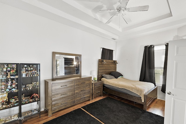 bedroom featuring a tray ceiling, ceiling fan, and light wood-type flooring