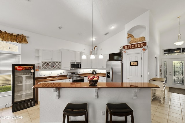 kitchen featuring appliances with stainless steel finishes, light tile patterned floors, white cabinets, and decorative light fixtures