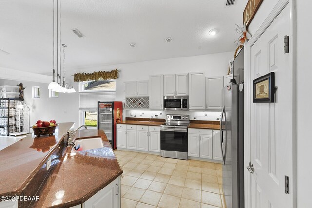 kitchen featuring appliances with stainless steel finishes, sink, white cabinets, and decorative light fixtures