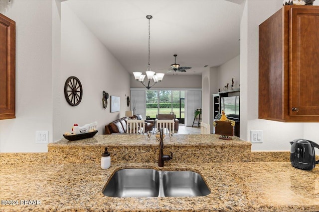 kitchen with pendant lighting, ceiling fan with notable chandelier, sink, and light stone counters