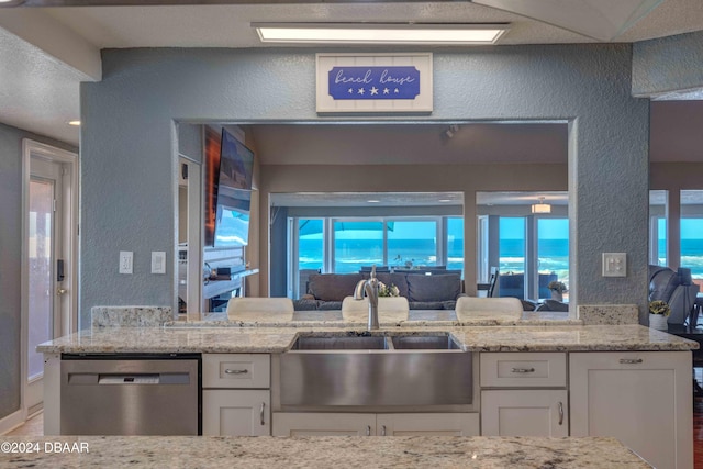 kitchen with light stone countertops, sink, stainless steel dishwasher, and white cabinets