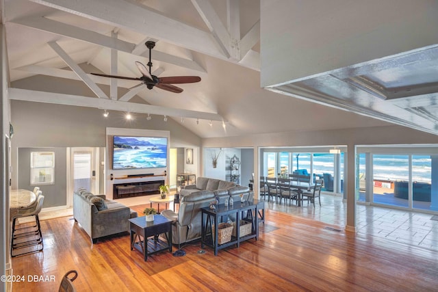 living room with a tile fireplace, hardwood / wood-style floors, high vaulted ceiling, ceiling fan, and beam ceiling