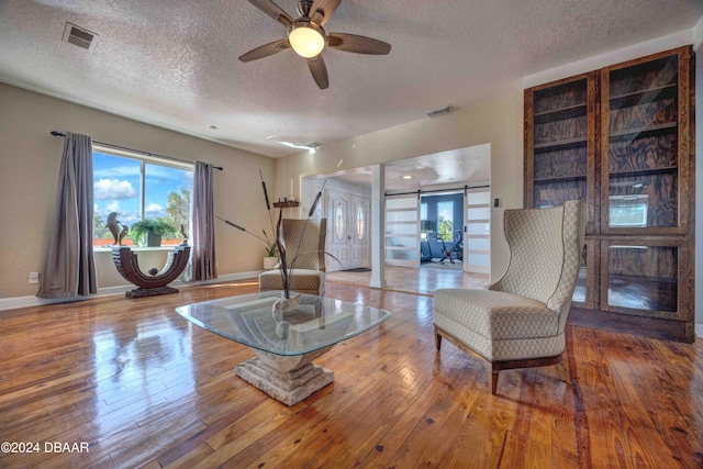 living area with hardwood / wood-style floors, a textured ceiling, a barn door, and ceiling fan