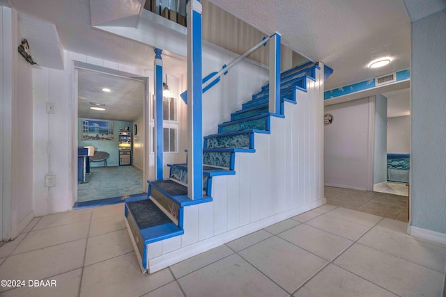 stairway with tile patterned floors and a textured ceiling