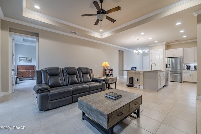 living room with ornamental molding, light tile patterned floors, sink, a tray ceiling, and ceiling fan with notable chandelier