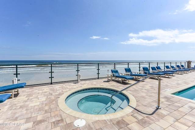 view of swimming pool featuring a patio area, a view of the beach, a water view, and a hot tub