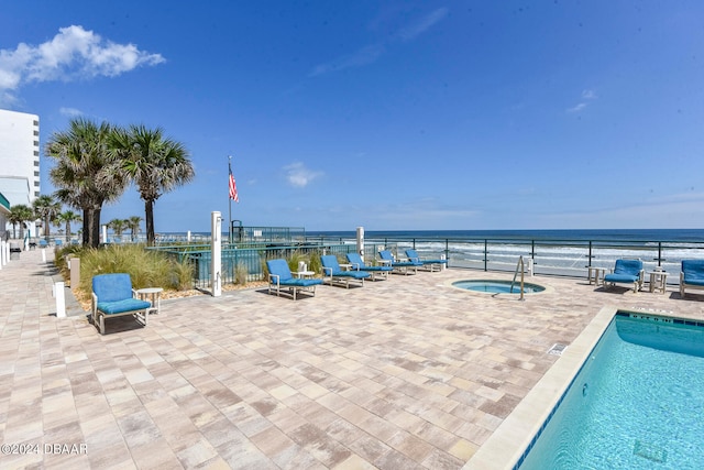 view of swimming pool featuring a hot tub, a water view, and a patio area