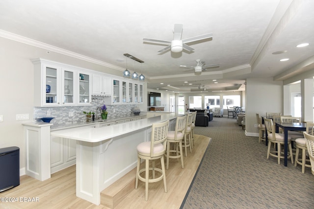 kitchen with ornamental molding, white cabinetry, light wood-type flooring, decorative light fixtures, and a breakfast bar area