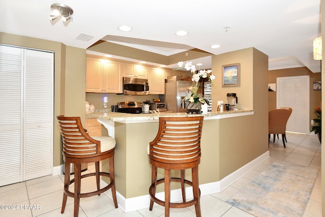 kitchen featuring light stone counters, appliances with stainless steel finishes, a kitchen bar, and light tile patterned flooring