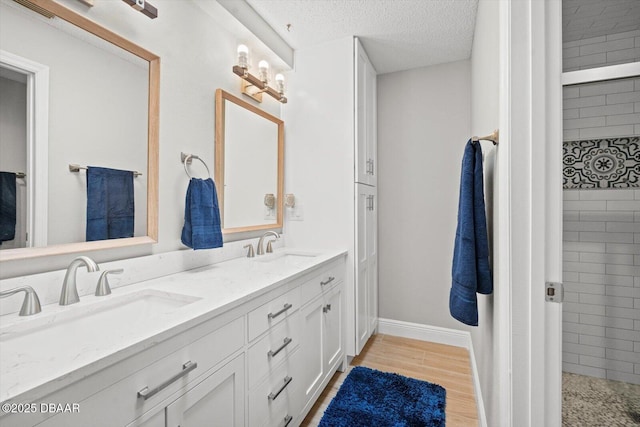 bathroom with wood finished floors, a sink, a textured ceiling, and double vanity