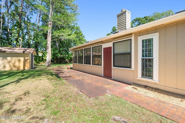 rear view of property with a lawn, a chimney, an outdoor structure, and a patio