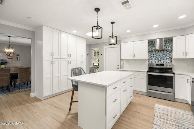 kitchen with wall chimney range hood, crown molding, stainless steel electric range, a kitchen bar, and visible vents