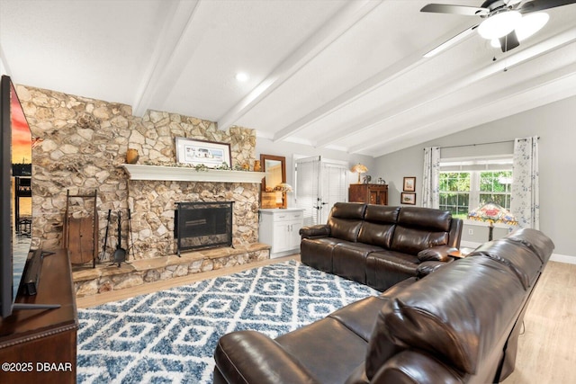 living area with vaulted ceiling with beams, baseboards, wood finished floors, ceiling fan, and a stone fireplace