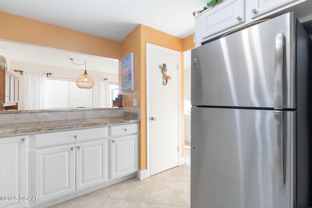 89 S Atlantic Ave Unit 1004, Ormond Beach, FL 32176 - kitchen with freestanding refrigerator, white cabinetry, light tile patterned flooring, light stone counters, and hanging light fixtures