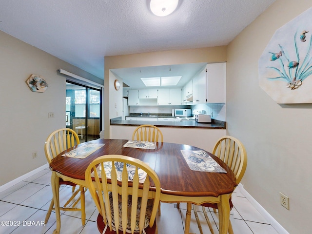 dining room featuring a textured ceiling, light tile patterned floors, and a skylight