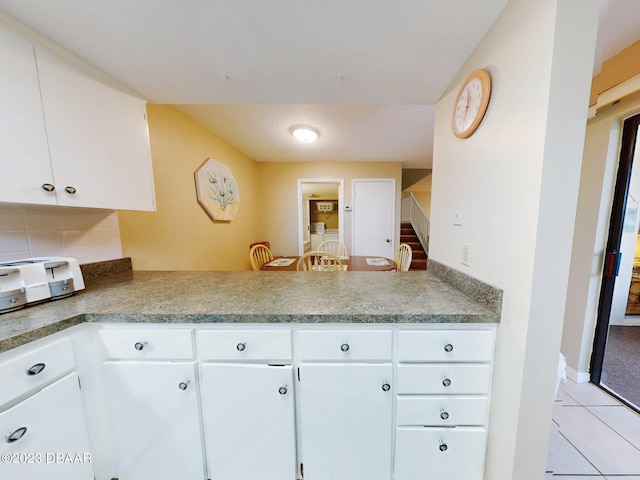 kitchen with white cabinetry, kitchen peninsula, light tile patterned floors, and tasteful backsplash