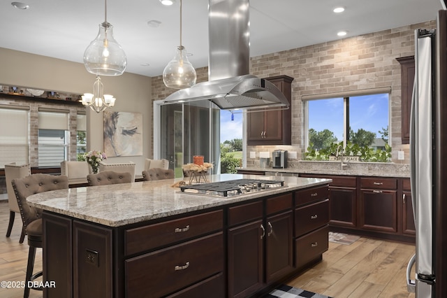 kitchen featuring light wood-style floors, a breakfast bar area, a center island, island exhaust hood, and appliances with stainless steel finishes