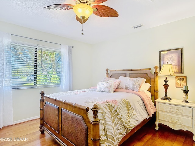 bedroom with ceiling fan, a textured ceiling, visible vents, baseboards, and light wood-style floors