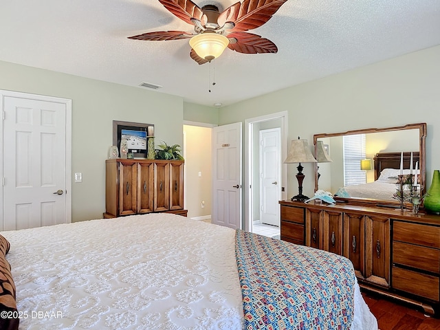 bedroom with a ceiling fan, visible vents, a textured ceiling, and wood finished floors