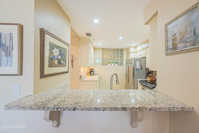 kitchen with kitchen peninsula, appliances with stainless steel finishes, light stone counters, and a kitchen breakfast bar