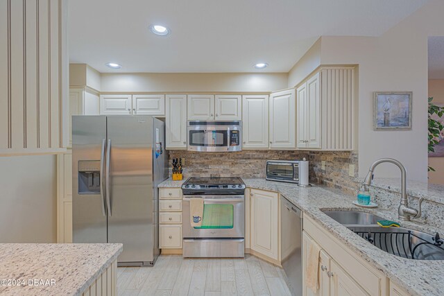 kitchen with light hardwood / wood-style floors, sink, tasteful backsplash, light stone countertops, and appliances with stainless steel finishes