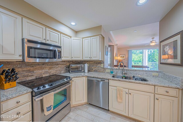 kitchen with tasteful backsplash, cream cabinets, appliances with stainless steel finishes, light stone countertops, and sink