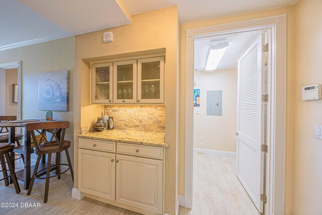 kitchen featuring electric panel, light stone counters, crown molding, decorative backsplash, and light hardwood / wood-style flooring