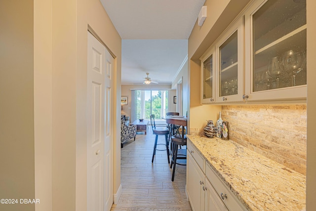 kitchen with white cabinets, ornamental molding, ceiling fan, light stone countertops, and light hardwood / wood-style flooring