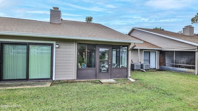 rear view of house featuring a lawn, central air condition unit, and a sunroom