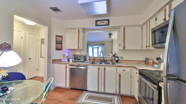 kitchen featuring light wood-type flooring, stainless steel appliances, white cabinetry, and sink