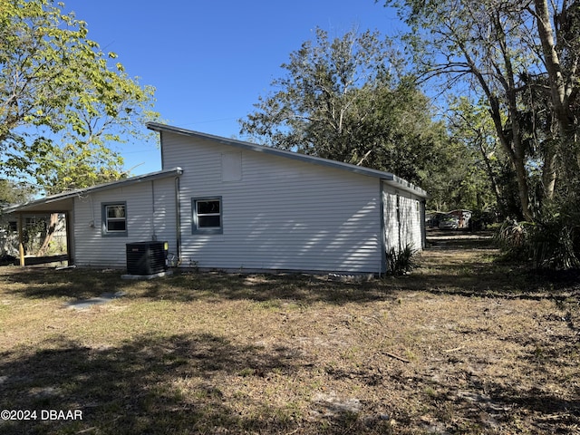 view of side of home with central AC unit, a carport, and a yard