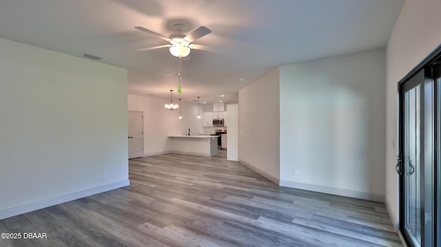 unfurnished living room with ceiling fan with notable chandelier and light wood-type flooring