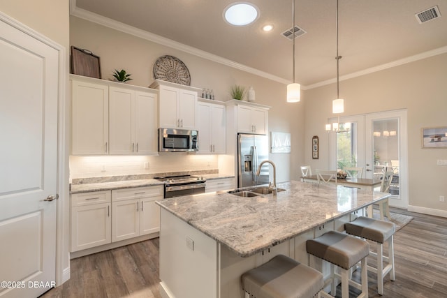 kitchen featuring sink, hanging light fixtures, appliances with stainless steel finishes, an island with sink, and white cabinets