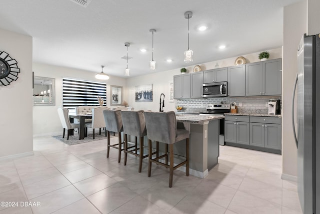 kitchen featuring light stone countertops, appliances with stainless steel finishes, gray cabinets, hanging light fixtures, and an island with sink