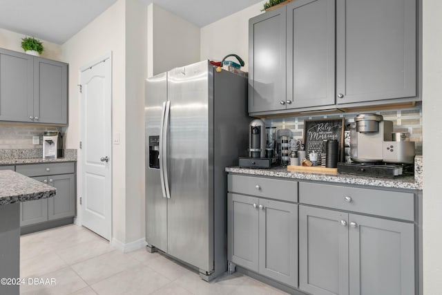 kitchen with stainless steel refrigerator with ice dispenser, gray cabinets, tasteful backsplash, light tile patterned flooring, and light stone counters