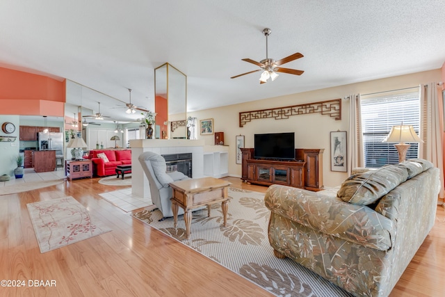 living room featuring light hardwood / wood-style floors, ceiling fan, and a tiled fireplace