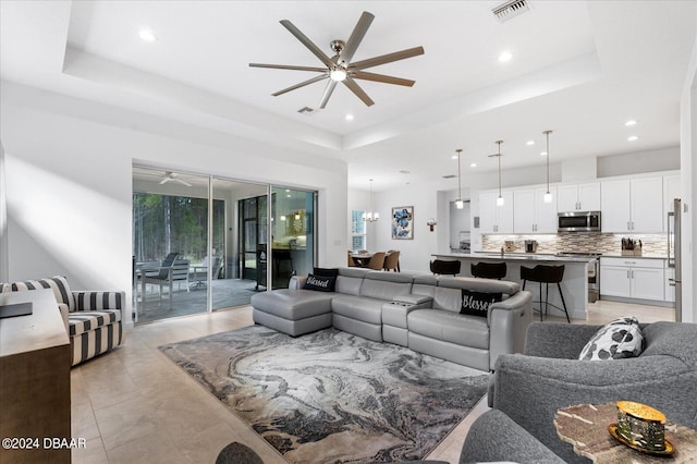 tiled living room featuring a tray ceiling and ceiling fan with notable chandelier