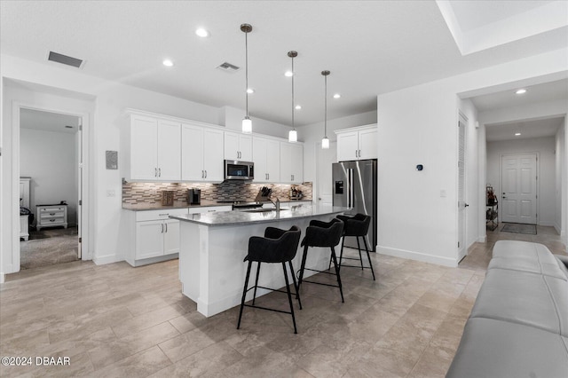 kitchen with a center island with sink, sink, white cabinetry, appliances with stainless steel finishes, and hanging light fixtures