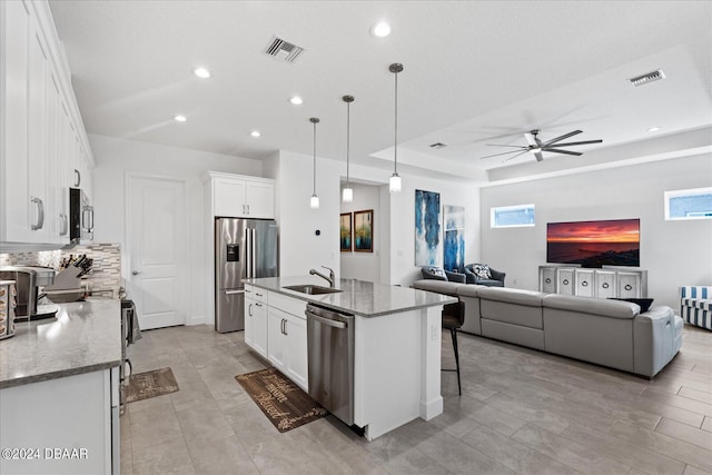 kitchen with white cabinetry, stainless steel appliances, a center island with sink, and decorative light fixtures