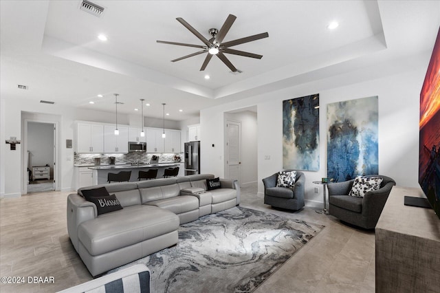 living room with a tray ceiling and ceiling fan