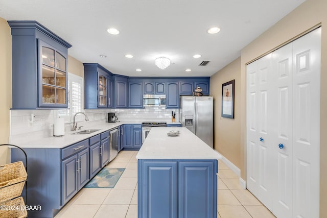 kitchen with appliances with stainless steel finishes, backsplash, blue cabinets, sink, and a kitchen island