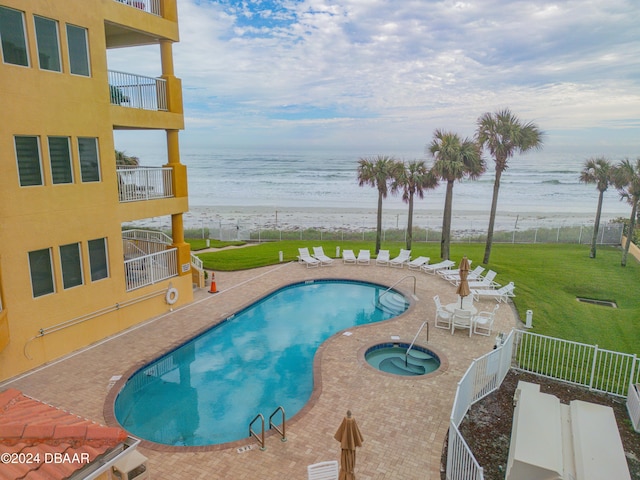 view of pool featuring a water view, a patio area, a beach view, a hot tub, and a lawn