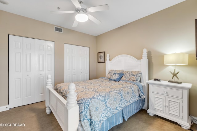 bedroom with dark colored carpet, ceiling fan, and multiple closets